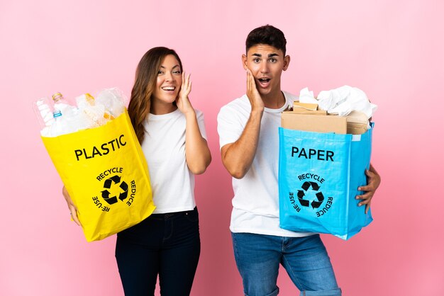 Jong koppel met een zak vol plastic en papier op roze met verbazing en geschokt gelaatsuitdrukking