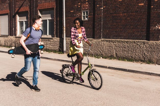 Foto jong koppel met fiets en skateboard wandelen in de straat