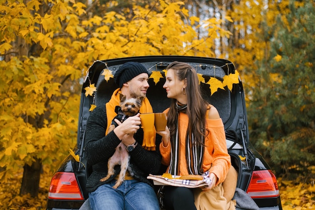 Jong koppel met hond zit in een auto kofferbak