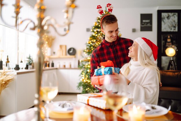 Jong koppel met kerstcadeaus thuis in de buurt van de kerstboom Romantische dag Feestdagen Oud en Nieuw