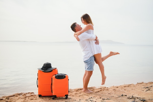 Jong koppel met koffer op het strand in zomerdag