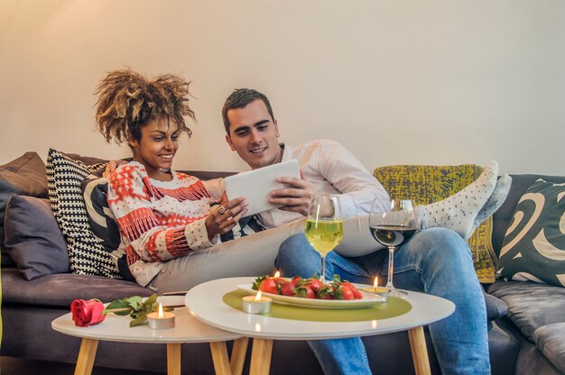 Jong koppel ontspannen in luxueus huis met tabletcomputers die in de woonkamer op de bankbank lezen.