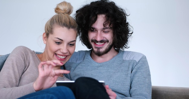 Foto jong koppel ontspannen in luxueus huis met tabletcomputers die in de woonkamer op de bankbank lezen.