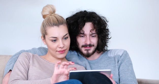 Foto jong koppel ontspannen in luxueus huis met tabletcomputers die in de woonkamer op de bankbank lezen.