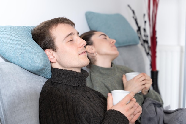 Jong koppel ontspannen met gesloten ogen en een warme kop koffie houden