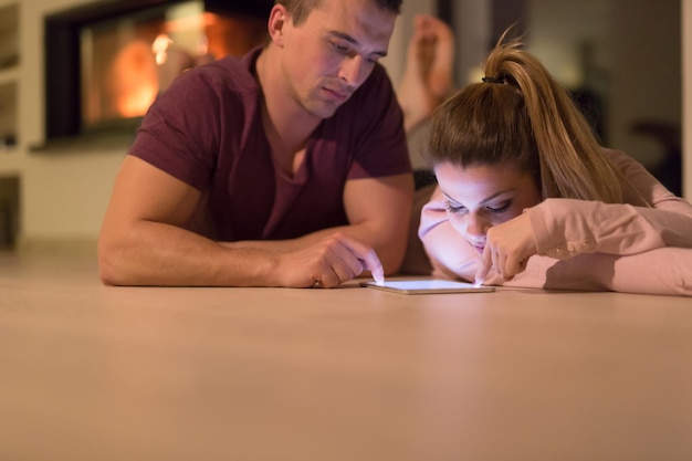 Jong koppel op de vloer voor open haard surfen op internet met behulp van digitale tablet op koude winternacht