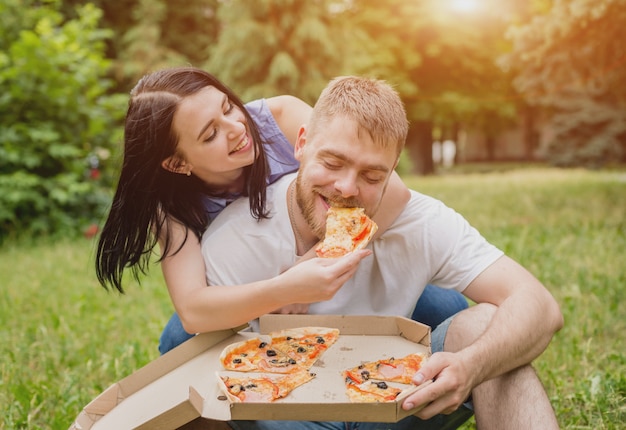 Jong koppel pizza eten in het park. Ze behandelen elkaar en lachen.