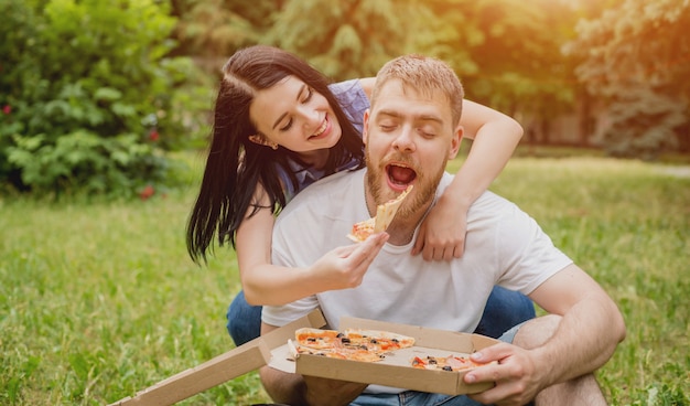 Jong koppel pizza eten in het park. Ze behandelen elkaar en lachen.