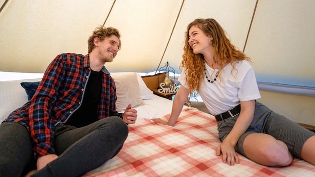 Jong koppel rustend op het bed in de tent bij glamping Glimlachen en lachen