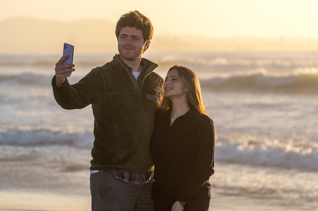 Jong koppel selfies nemen op het strand bij zonsondergang