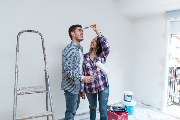 Jong koppel tussen verschillende rassen spelen met tekengereedschappen tijdens de renovatie van zijn appartement. Witte muur op de achtergrond in de woonkamer.