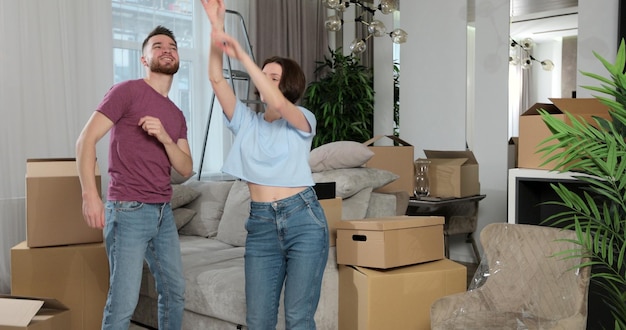 Jong koppel veel plezier met dansen in hun nieuwe appartement Gelukkige familie danst in nieuw appartement tussen veel kartonnen dozen die genieten van een verhuisdag