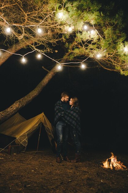 Jong koppel verliefd camping toeristen zitten bij een vuur tegen een tent in het bos met een retro slinger foto met veel lawaai selectieve focus