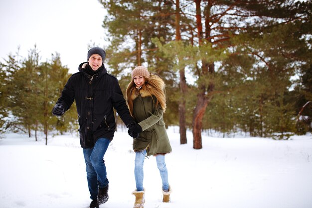 Jong koppel verliefd uitgevoerd en hand in hand in het besneeuwde winterbos