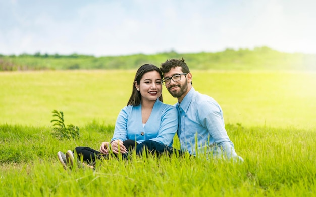 Jong koppel verliefd zittend op het gras kijken naar de camera Twee geliefden zittend op het gras kijken naar de camera Portret van een verliefd paar zittend op het gras in het veld