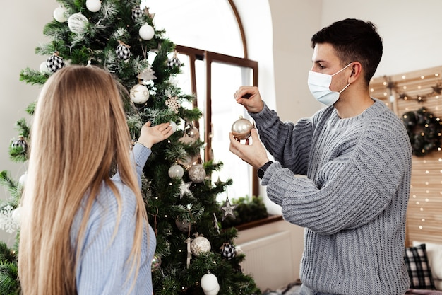 Jong koppel versieren kerstboom thuis dragen gezichtsmaskers close-up