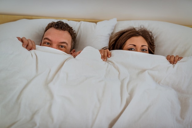 Jong koppel verstopt achter deken in bed.