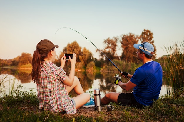 Jong koppel vissen en thee drinken op de rivier bij zonsondergang