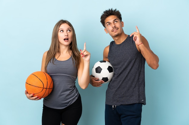 Jong koppel voetballen en basketballen op blauw denken een idee met de vinger omhoog