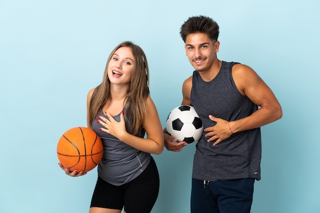 Jong koppel voetballen en basketballen op blauw lachend veel terwijl handen op de borst