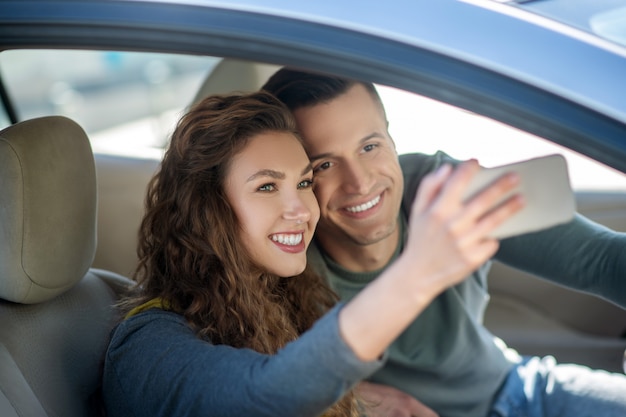 Jong koppel zitten in de auto, selfie maken en glimlachen