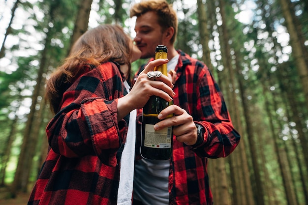 Jong koppel zoenen in het bos en houden een fles champagne in hun handen