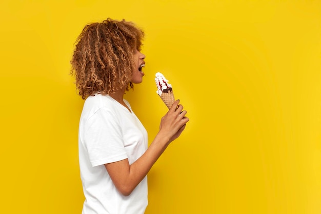 jong krullend Amerikaans meisje met beugels eet zoete ijs met jam op gele geïsoleerde achtergrond