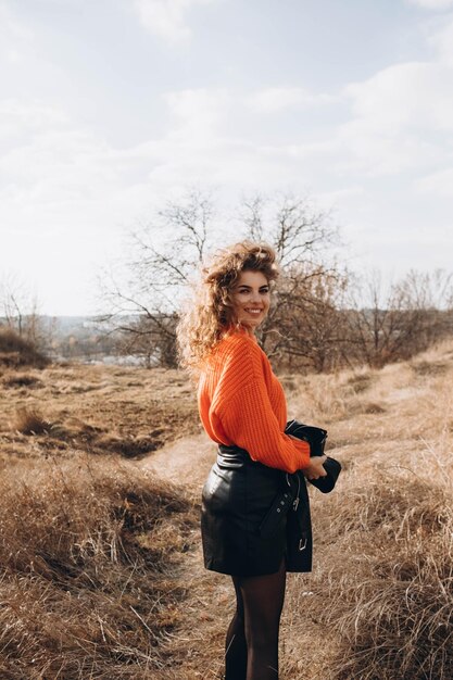 Jong krullend meisje in een oranje trui tegen de achtergrond van de herfstnatuur