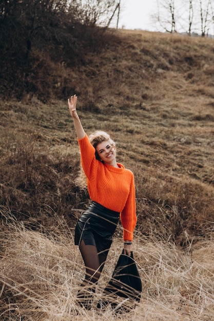 Foto jong krullend meisje in een oranje trui tegen de achtergrond van de herfstnatuur