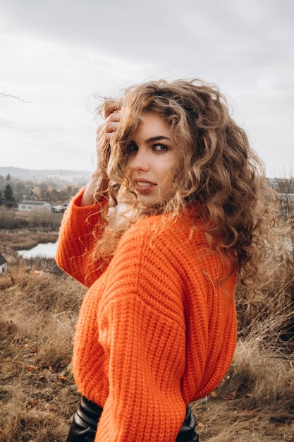 Foto jong krullend meisje in een oranje trui tegen de achtergrond van de herfstnatuur