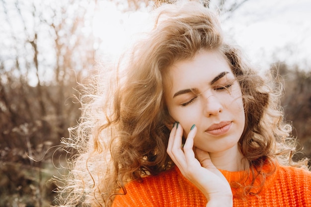 Foto jong krullend meisje in een oranje trui tegen de achtergrond van de herfstnatuur