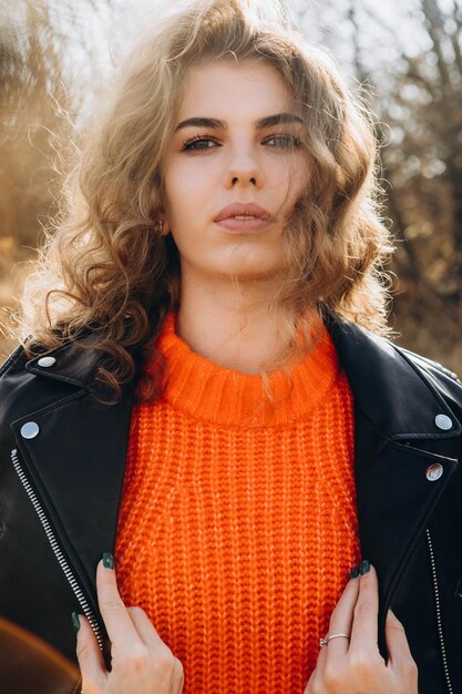 Foto jong krullend meisje in een oranje trui tegen de achtergrond van de herfstnatuur