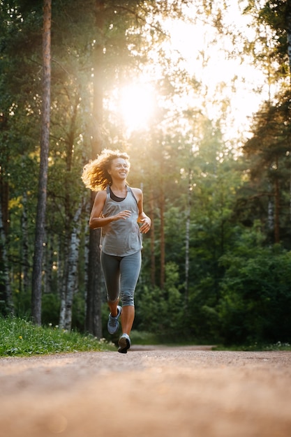 Jong krullend meisje loopt vrolijk een marathon op een bosweg bij zonsopgang gezonde levensstijl