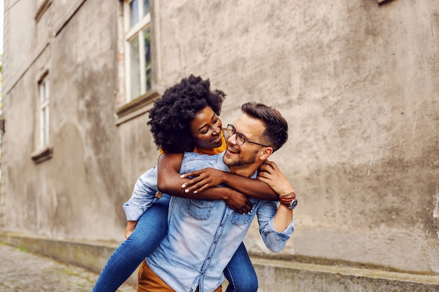 Jong lachend dolblij multicultureel hipsterpaar dat op de rug in openlucht heeft.