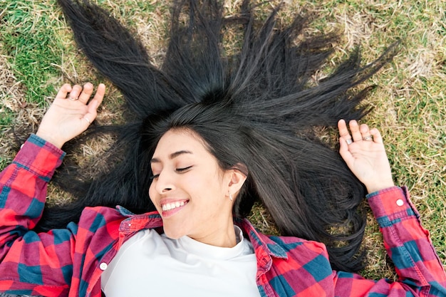 Jong lachend Latina-meisje dat buiten ligt met haar haar in het gras