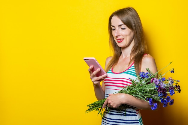 Jong lachend meisje kijkt naar de telefoon, houdt een boeket van wilde bloemen