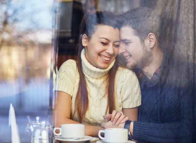 Jong lachend paar, zittend in het café, knuffelen en koffie drinken.