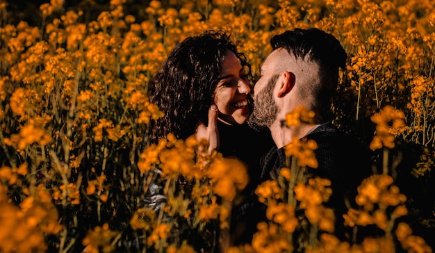 Jong lachend stel staat op het punt te kussen te midden van een veld met oranje bloemen in de lente