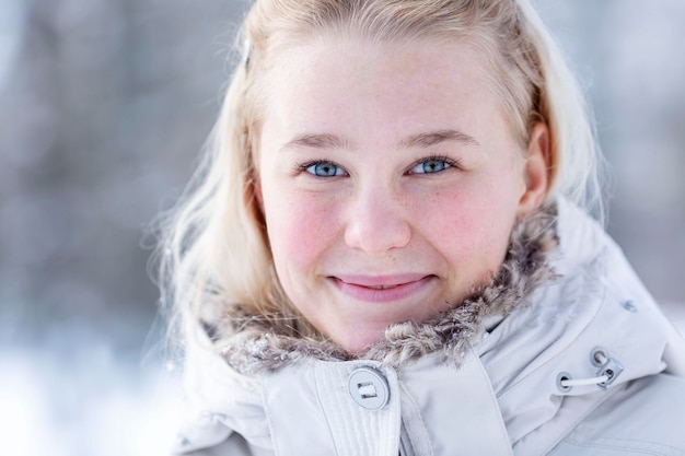 Jong lachend tienermeisje in een besneeuwd park Schattige blonde in een witte jas Wandelen in de frisse lucht in de winter en koude seizoenen Close-up