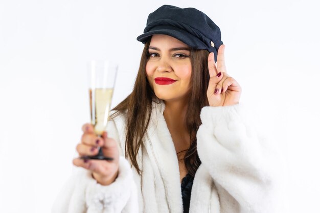 Jong Latijns meisje met zwarte hoed vieren oudejaarsavond op een witte achtergrond. Portret met een glas champagne