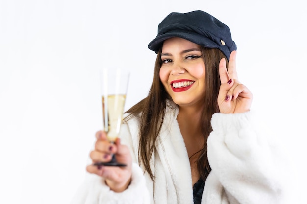 Jong Latijns meisje met zwarte hoed vieren oudejaarsavond op een witte achtergrond. Portret met een glas champagne