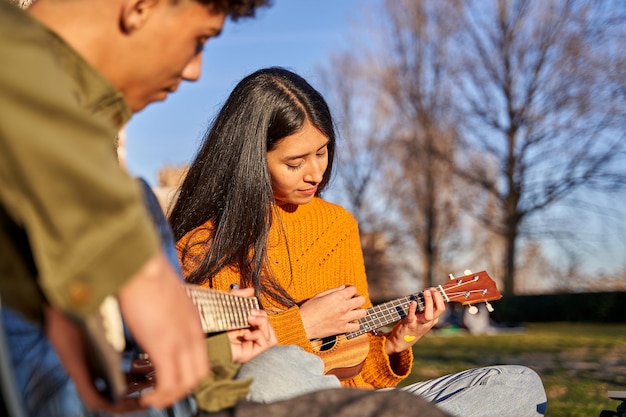 Jong latijns stel dat muziekinstrumenten bespeelt in het park, hij speelt een gitaar en zij speelt een ukelele