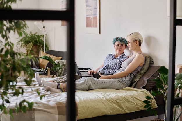 Jong lesbisch koppel dat samen een laptop gebruikt terwijl ze op bed in de slaapkamer liggen