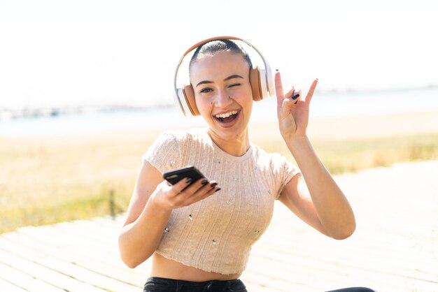 Jong Marokkaans meisje dat buiten muziek luistert met een mobiele telefoon die een rockgebaar maakt