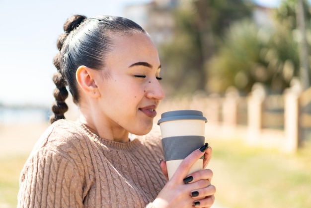 Jong Marokkaans meisje dat buitenshuis een afhaalkoffie vasthoudt met een gelukkige uitdrukking