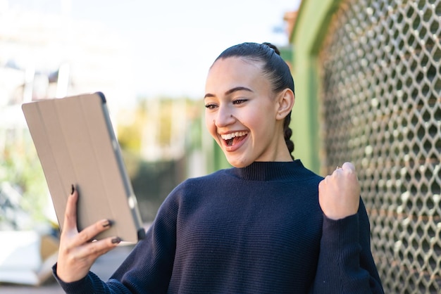 Jong Marokkaans meisje dat buitenshuis een tablet vasthoudt en een overwinning viert