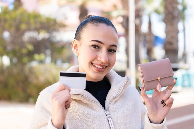 Jong Marokkaans meisje dat in openlucht portefeuille en creditcard met gelukkige uitdrukking houdt