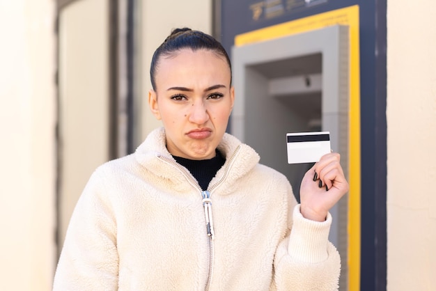 Jong Marokkaans meisje met een creditcard buitenshuis met een droevige uitdrukking