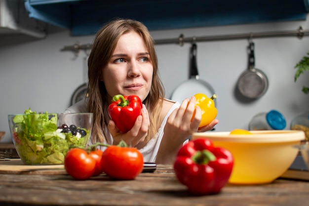 Jong meisje bereidt een vegetarische salade in de keuken, ze kiest voor rode of gele paprika