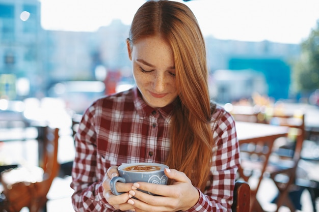 Jong meisje dat aan een kop van koffie het glimlachen kijkt